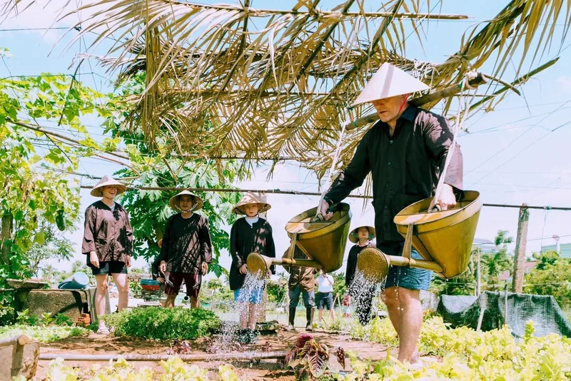 Du khách đội nón lá trải nghiệm tưới rau bằng gánh nước truyền thống tại làng rau Trà Quế gần Hội An.