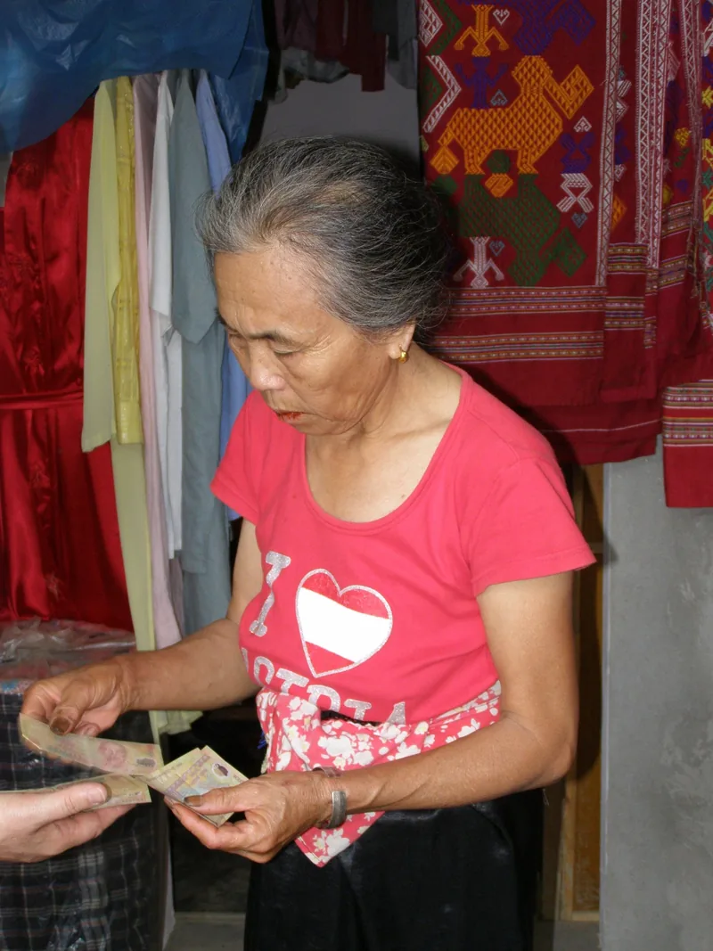 Một người bán hàng cao tuổi đang đếm tiền trước những tấm vải dệt thổ cẩm ở Mai Châu.