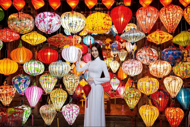 Người phụ nữ mặc áo dài trắng đứng giữa những chiếc đèn lồng lụa sặc sỡ ở Hội An.