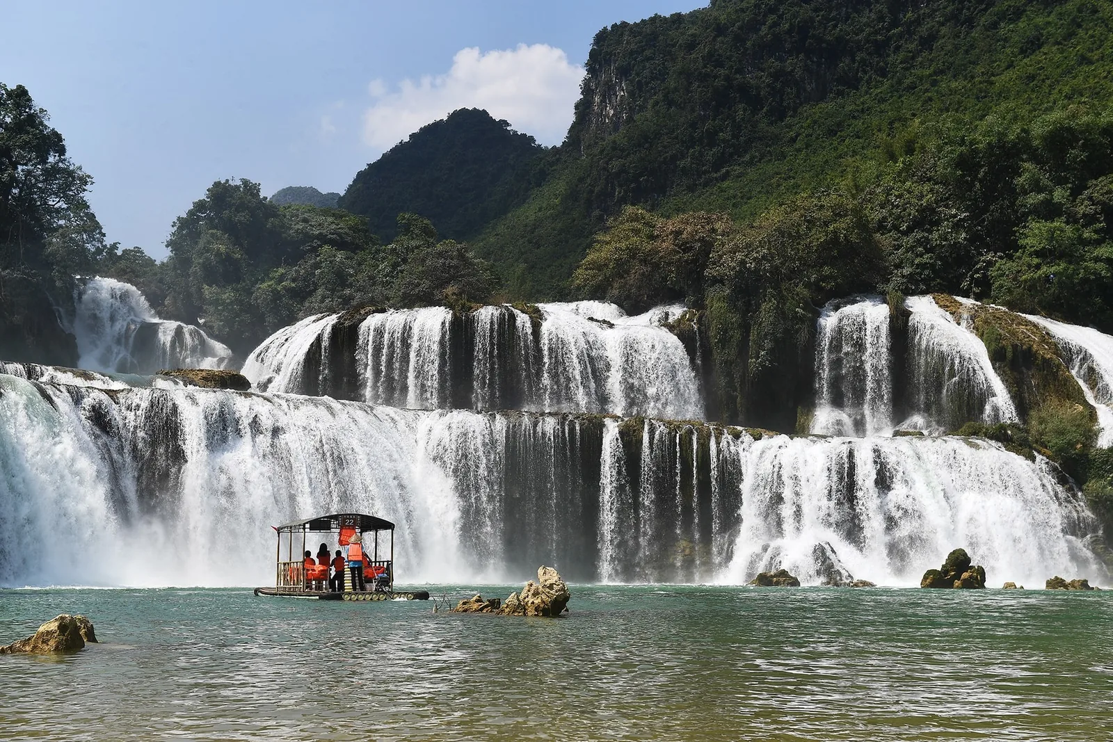 Một chiếc bè tre chở du khách trên hồ nước xanh dưới chân thác Bản Giốc nhiều tầng ở Cao Bằng.