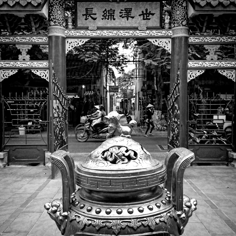 Lư hương chạm khắc tinh xảo đặt trước cổng đền, nhìn ra con phố Việt Nam nhộn nhịp xe máy.